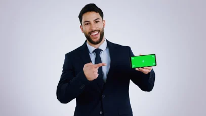 Professional businessman in dark suit pointing at smartphone with green screen display, presenting MyGreenBucks financial app against gray studio background